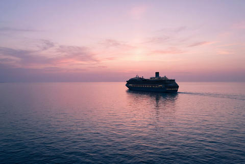Cruise ship sailing on a calm ocean toward a pink and purple sunset