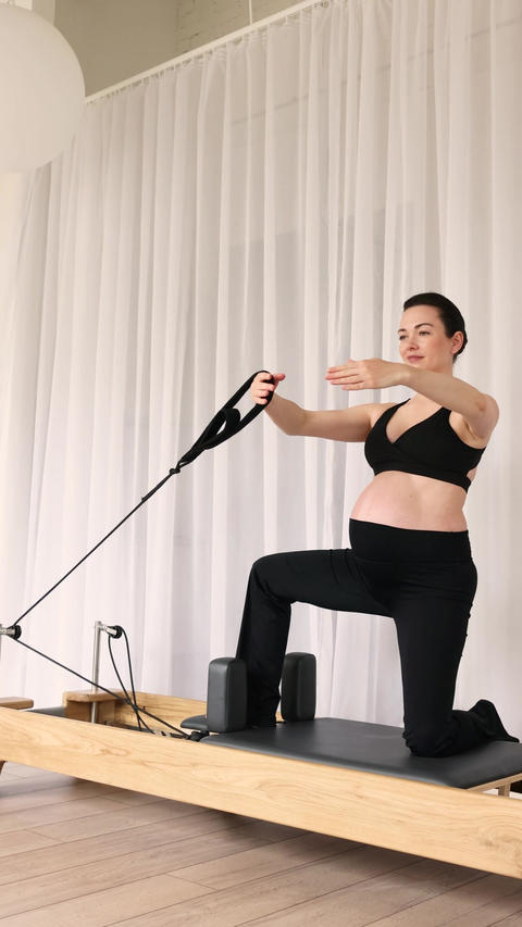 Pregnant woman exercising on Pilates reformer machine during healthy pregnancy