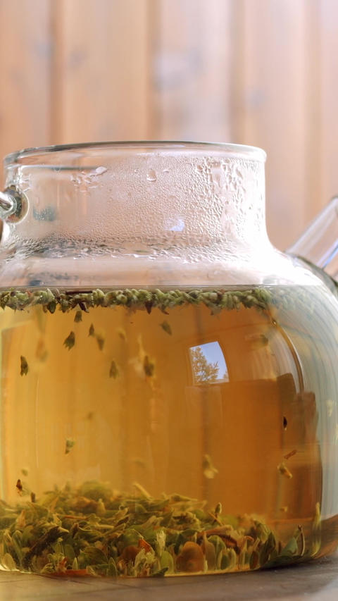 Glass teapot with herbal tea steeping slowly, clear amber infusion with floating