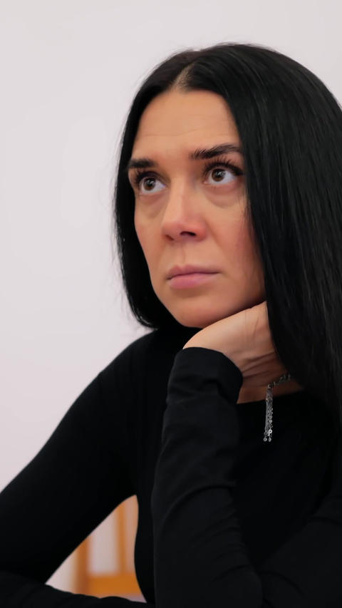 Woman in black shirt adjusts neck and arm while seated, shifting pose through