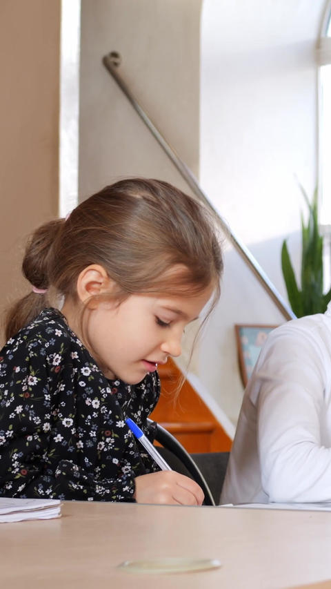Schoolchildren write in classroom during lesson, seated at desks near bright