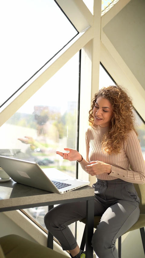 Young woman having a happy video call on a laptop in a cafe