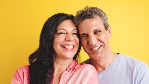 Middle aged couple smiling in studio with yellow background