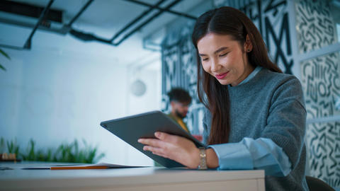 Contemporary office interior with wall decor. Asian woman holding tablet device and tapping screen