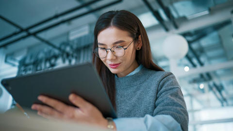 Asian female student wearing glasses holding tablet with one hand. Reading lecture slides on
