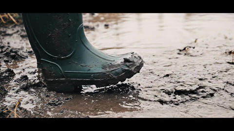 Close Up Of Dark Green Rubber Boots Stepping And Splashing In Thick Muddy Water