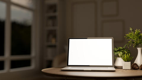 White screen laptop and acorn with vase and green pot plants on wooden table in a dim lit living roo