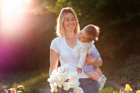 Summertime. Portrait of caucasian happy mother holding bouqet of irises and her cute baby at arms.