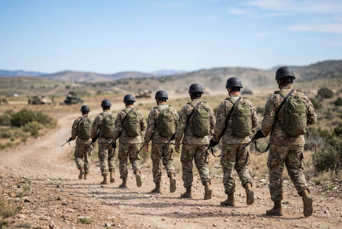 Squad of military personnel walking along a dirt path during training