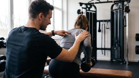 Personal Trainer Guiding Row Technique Over Shoulder In Quiet Gym