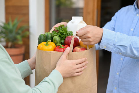 Courier handing a paper bag of groceries to a customer