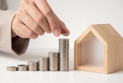 Property Investment Concept With Hand Placing Silver Coins Near A Wooden House Model
