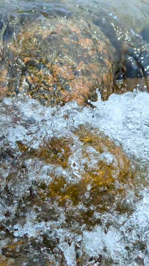 Closeup of a river rock partially submerged in flowing water with natural surroundings