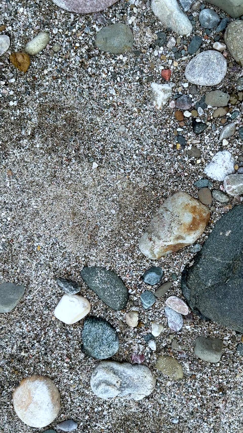 Closeup of assorted pebbles and stones on a sandy beach with diverse textures and natural colors