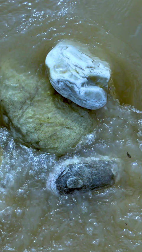 Closeup of smooth stones submerged in flowing water with a natural earthy color palette