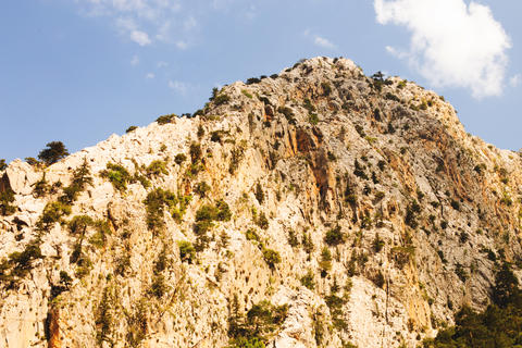 Scenic view of a steep, rocky mountain with trees and shrubs, set against a vibrant blue sky