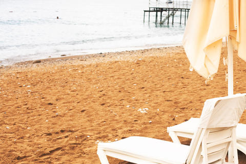 Beach scene with empty closed umbrellas and sun loungers on on sea shore