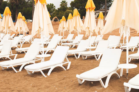 Beach scene with empty closed umbrellas and sun loungers on on sea shore
