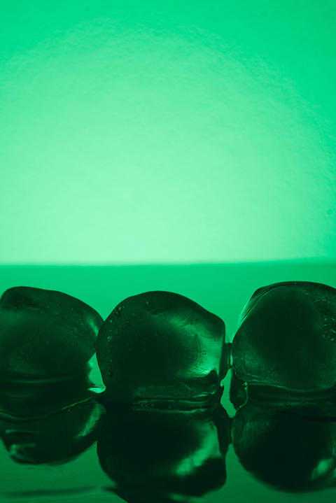 Pure clean Ice Cubes Melting On Mirror Surface In Neon Green Light Still Life