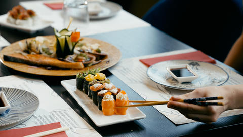 Person eating salmon nigiri with chopsticks at sushi restaurant