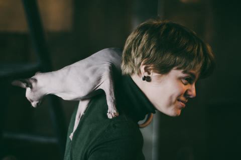 Portrait young woman with bald cat on shoulders, authentic photography in home