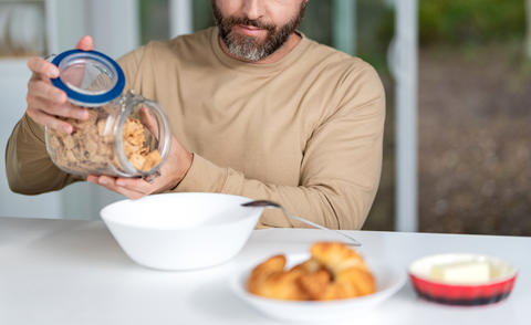 Man cropped view put cereal flakes for breakfast at home kitchen, healthy food