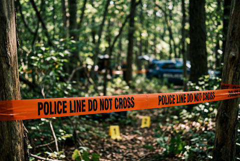 Orange police line do not cross tape in woods with evidence markers