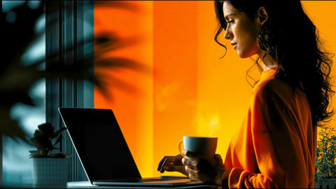 Woman works remotely on a laptop while holding a steaming cup