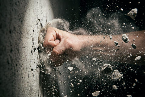 Powerful fist punching concrete wall with flying debris