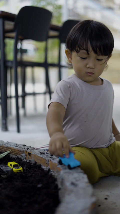 Toddler Boy Playing With Toy Car In Potting Soil At The Garden 06