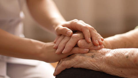 Young caregiver's hands gently holding an elderly person's hands