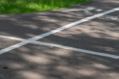 Close-up view of painted white crossing lines on weathered asphalt path with dappled sunlight, soft