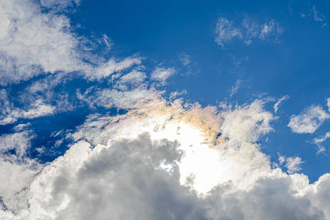 Sunlit iridescent cirrus clouds displaying atmospheric diffraction beneath towering cumulus formatio
