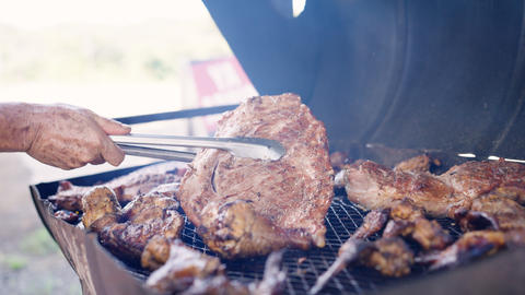 Hand flipping large meat cut on barbecue grill
