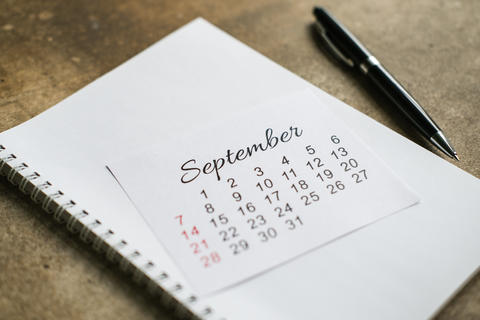 September calendar page on white spiral notebook and black pen on concrete background. Business