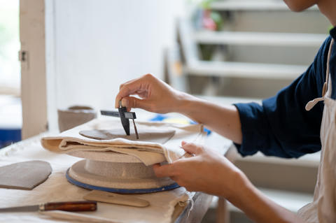 Pottery artist using compass cut clay into circle on throwing wheel at work table in class or studio