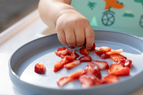 Baby hand picking up strawberries from plate