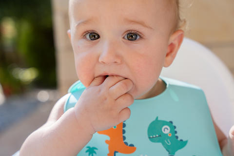Baby boy teething chewing fingers wearing bib