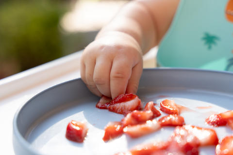 Baby hand picking up strawberries from plate