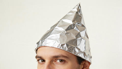 suspicious looking man wearing tinfoil hat believing conspiracy theory