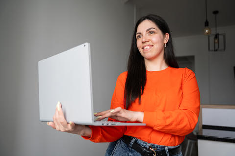 Smiling woman holding laptop presenting online in home office environment. Remote work digital produ