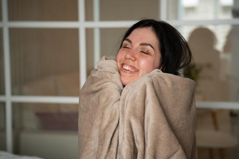 Woman wrapped in a cozy blanket smiling inside a modern home. Winter comfort and home heating during