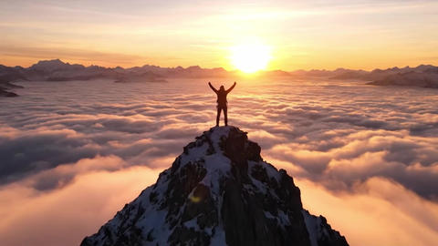 Hiker's triumph on a mountain peak above the clouds. Epic drone reveal