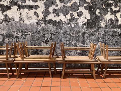 Rows of long wooden benches stored on brown tiled floor beside school wall