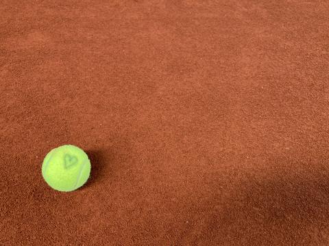 tennis ball with a hand-drawn heart resting on a clay court