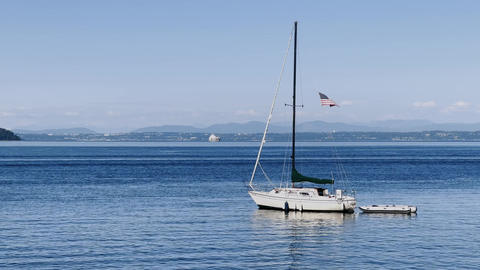 Sailboat anchored on calm blue water with a small dinghy and American flag