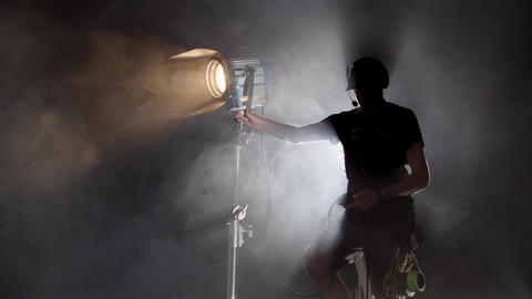Lighting Technician Aiming Fresnel Spotlight Toward Camera