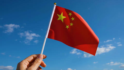 Hand Holding Chinese Flag Waving On Blue Sky for National Pride Patriotism and Cultural Identity