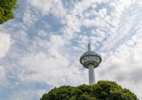 Modern Broadcasting Tower Rising Above Green Trees Against a Partially Cloudy Sky