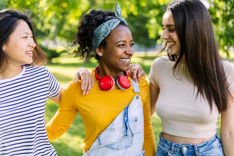 Three young women walking and laughing together in a park